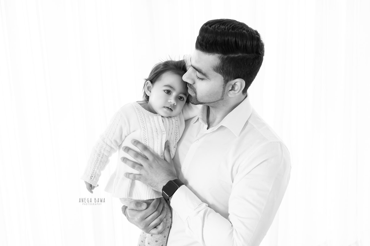 1-year-old girl posing with dad against a white backdrop, photographed by Anega Bawa Photography for a family photoshoot in Gurgaon (Delhi NCR).