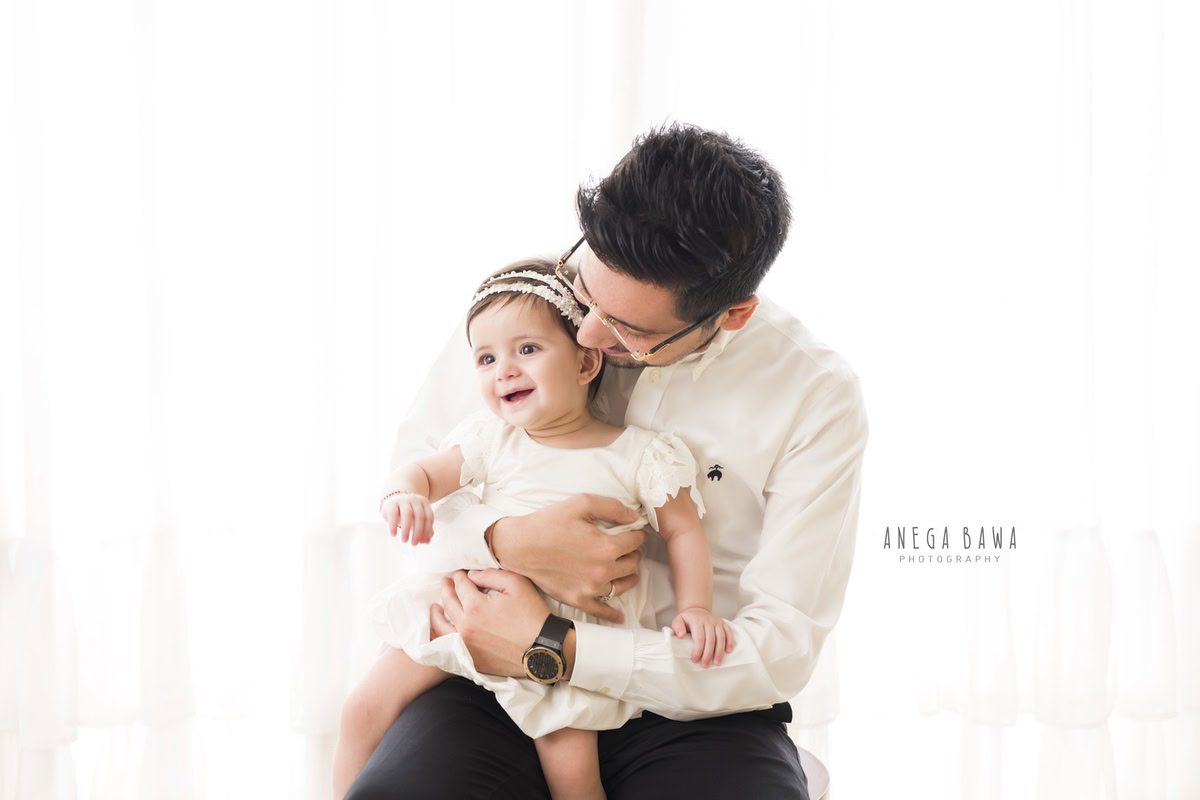 1-year-old girl posing with dad against a white backdrop, captured by Anega Bawa, family photographer in Gurgaon (Delhi NCR).