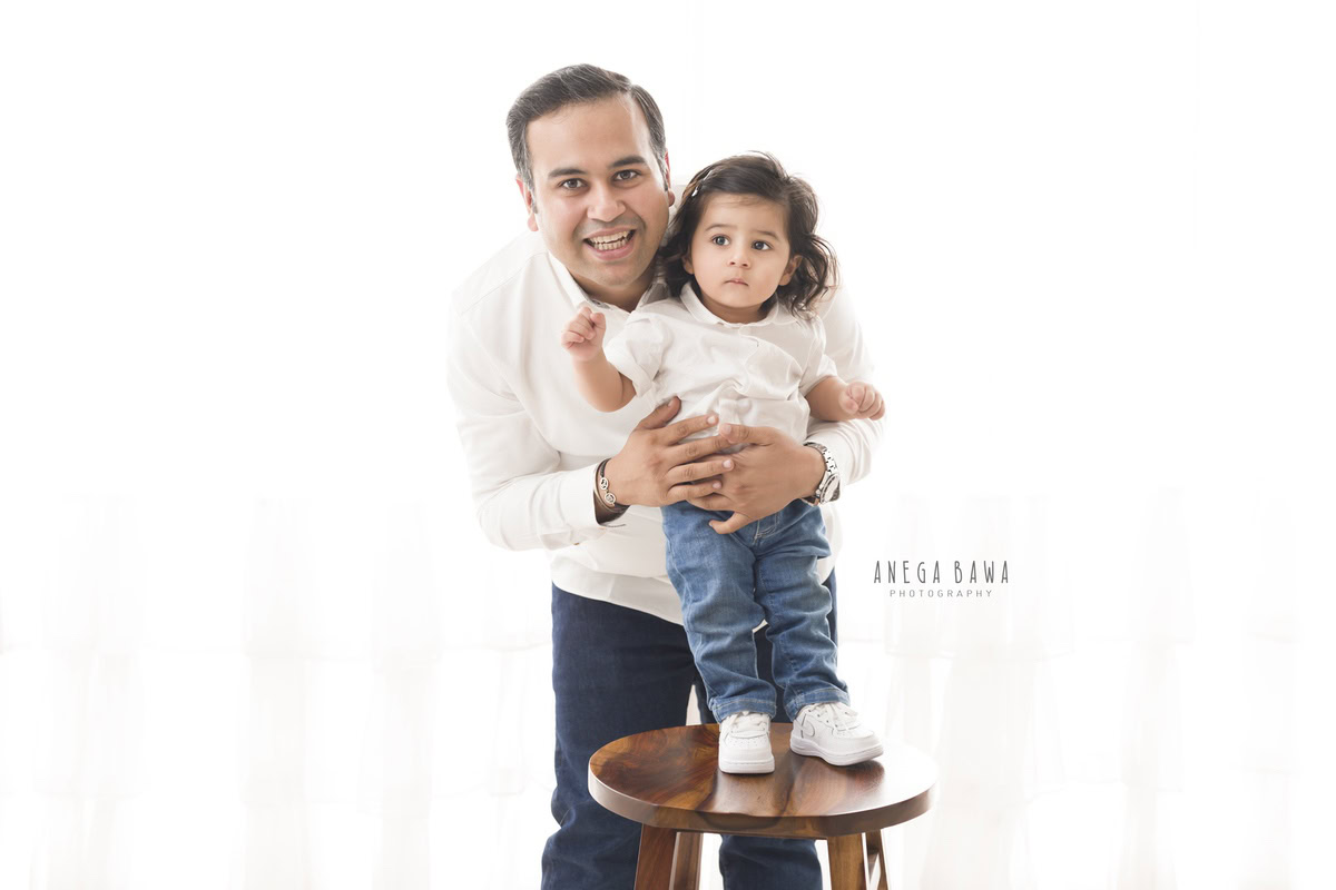1-year-old girl posing with dad against a white backdrop, captured by Anega Bawa Family Photographer Gurgaon (Delhi NCR).
