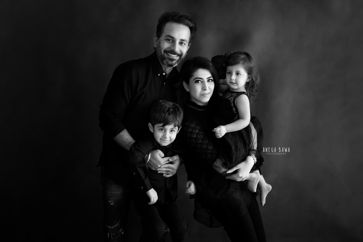 1-year-old girl posing with her elder brother, mom, and dad against a black and white backdrop, captured by Anega Bawa Family Photographer Gurgaon (Delhi NCR).