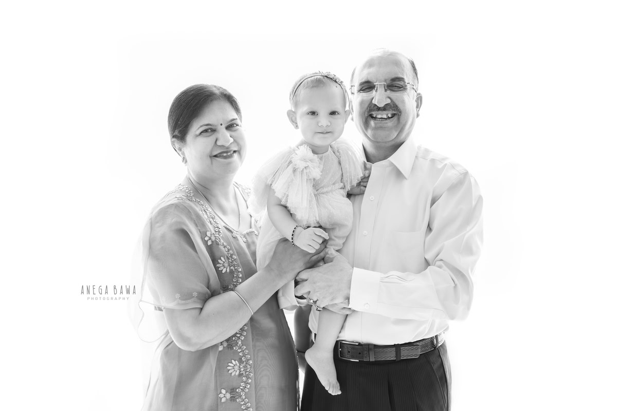 1-year-old girl posing with grandparents in a black and white pose against a white backdrop. Captured by Anega Bawa Photography for a family photoshoot in Gurgaon (Delhi NCR).