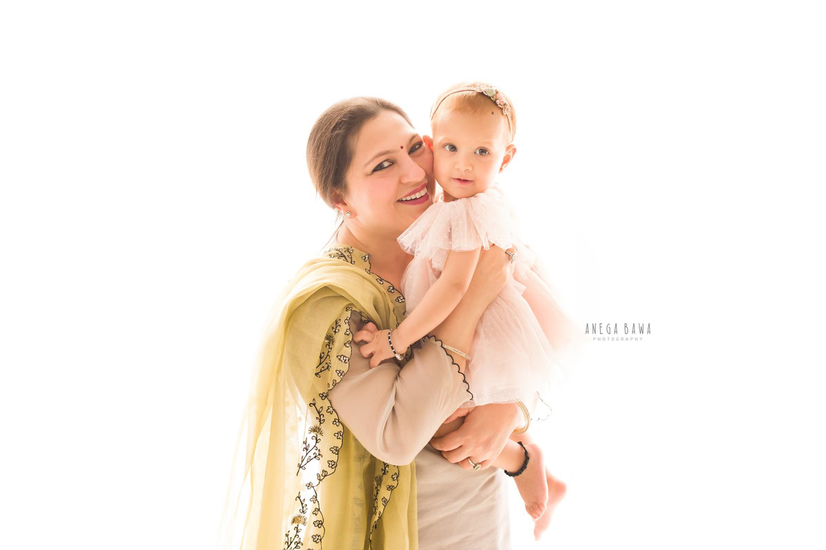 1-year-old girl posing with granny against a white backdrop, captured by Anega Bawa, family photographer in Gurgaon (Delhi NCR).