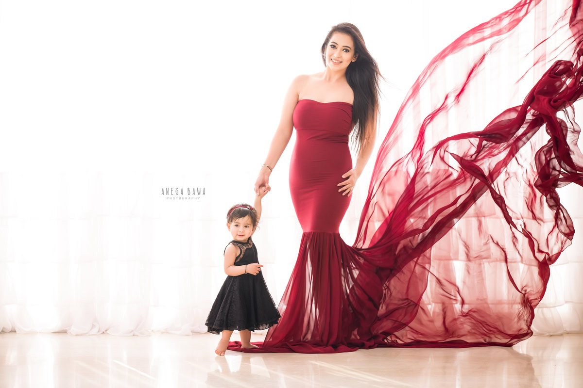1-year-old girl posing with mom in a red dress against a white backdrop, captured by Anega Bawa Family Photographer Gurgaon (Delhi NCR).