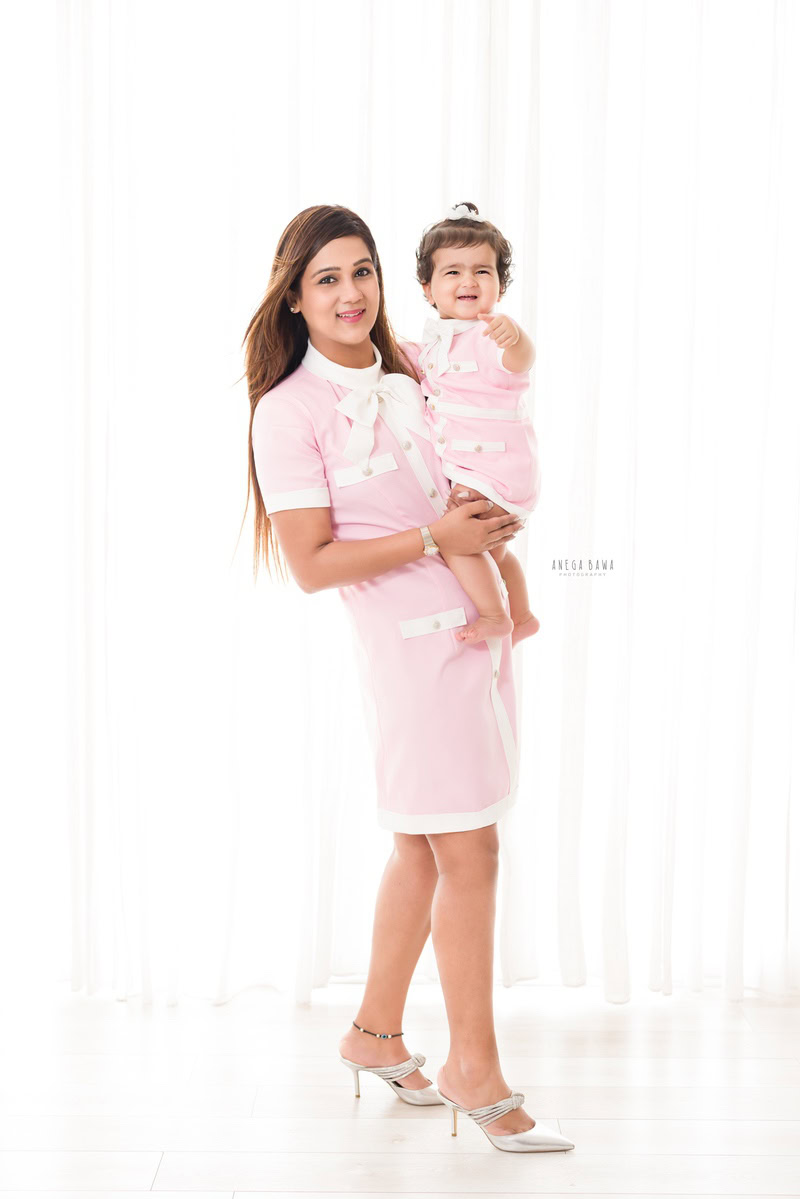 1-year-old girl posing with mom in a cute baby pink dress against a white backdrop. Captured beautifully by Anega Bawa Photography for a family photoshoot in Gurgaon (Delhi NCR).