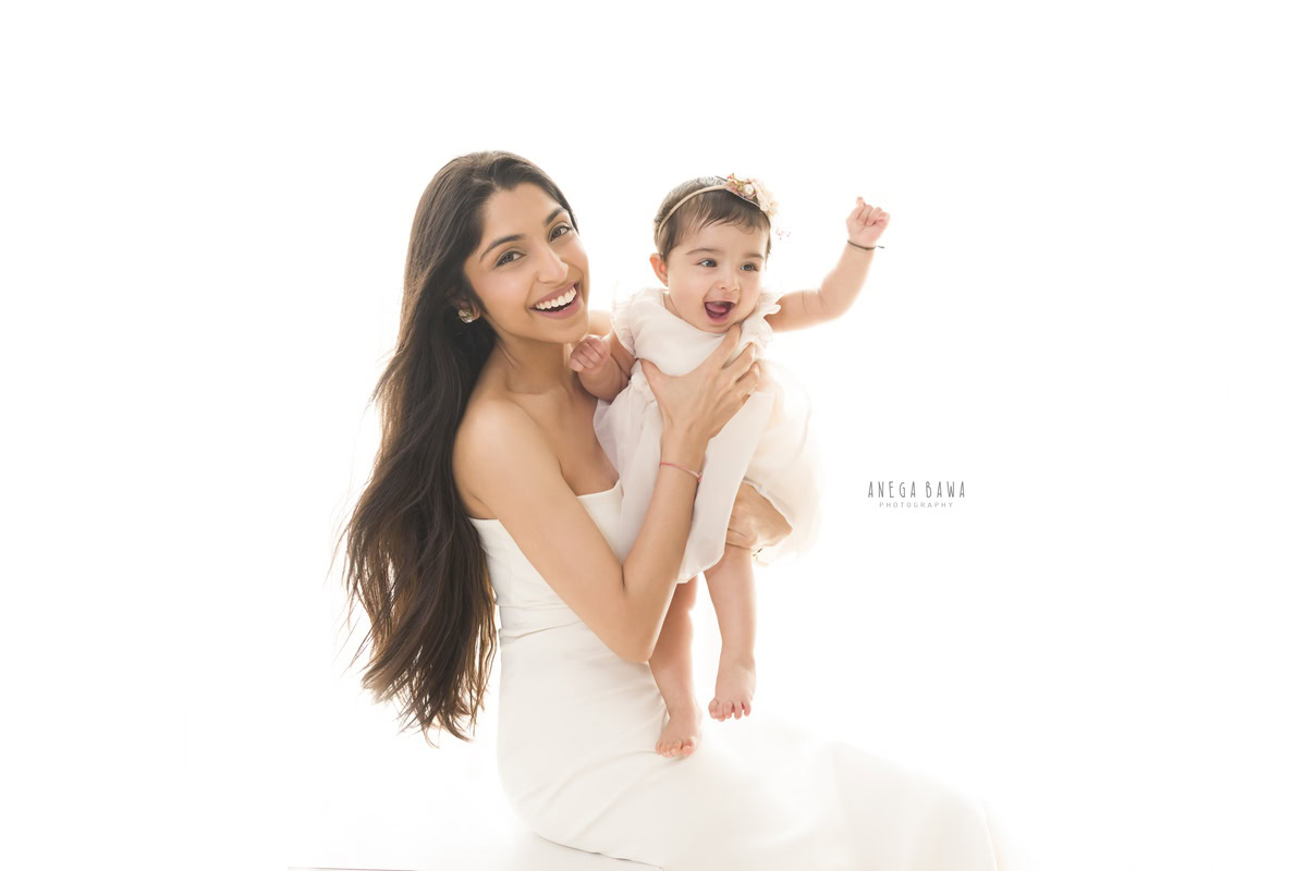 1-year-old girl posing with mom in a cute laughing pose against a white backdrop, captured by Anega Bawa, family photographer in Gurgaon (Delhi NCR).