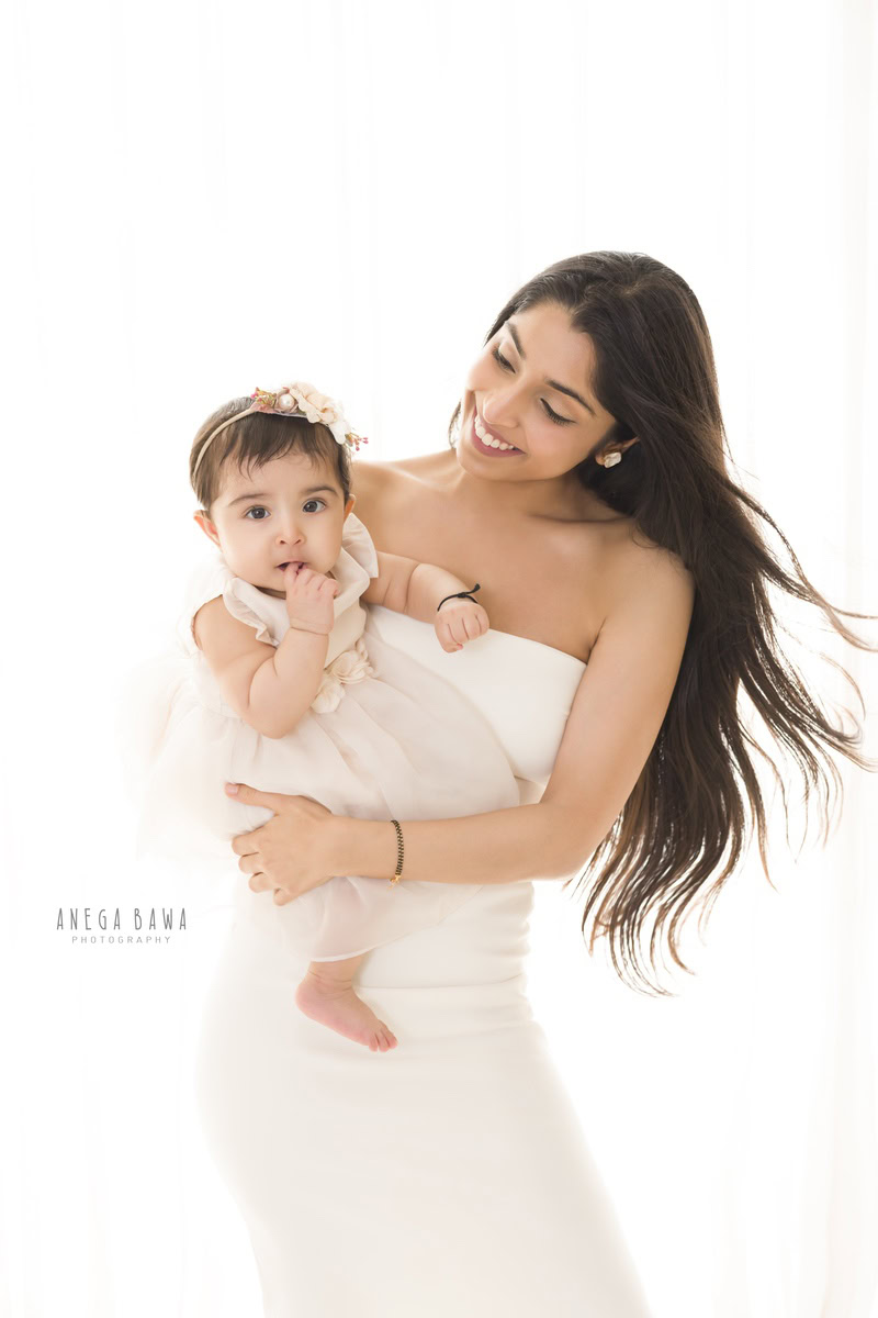 1-year girl posing with mom in a cute white dress against a white backdrop, captured by Anega Bawa Photography in Gurgaon (Delhi NCR).