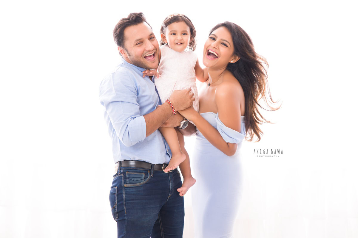 1-year-old girl posing with mom and dad, all smiling against a white backdrop, captured by Anega Bawa Family Photographer Gurgaon (Delhi NCR).