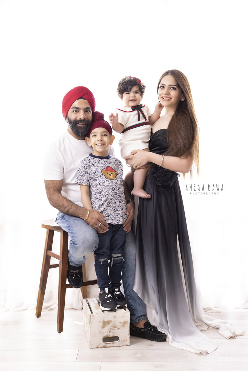 1-year-old girl posing with mom, dad, and elder brother in a smiling family pose against a white backdrop, captured by Anega Bawa Family Photographer Gurgaon (Delhi NCR).