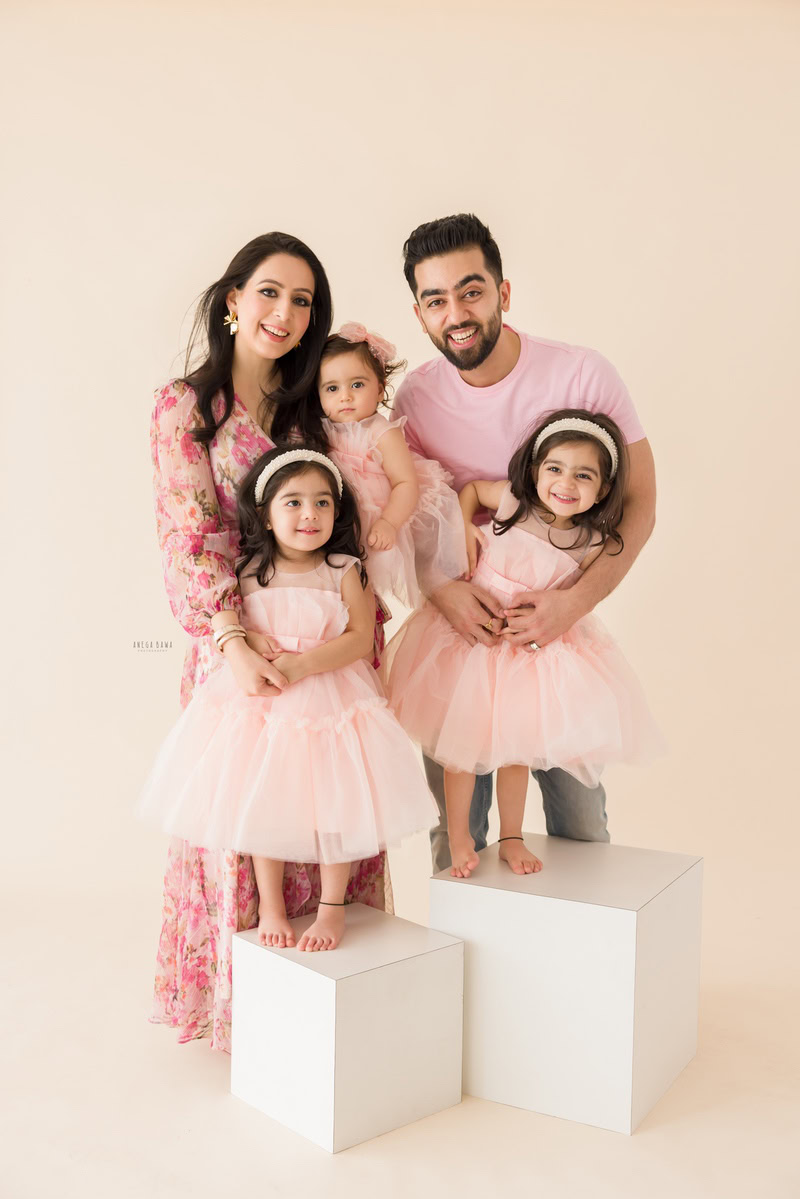 1-year-old girl posing with mom, dad, and twin sisters in a family pose against a serene peach-shaded beige backdrop.