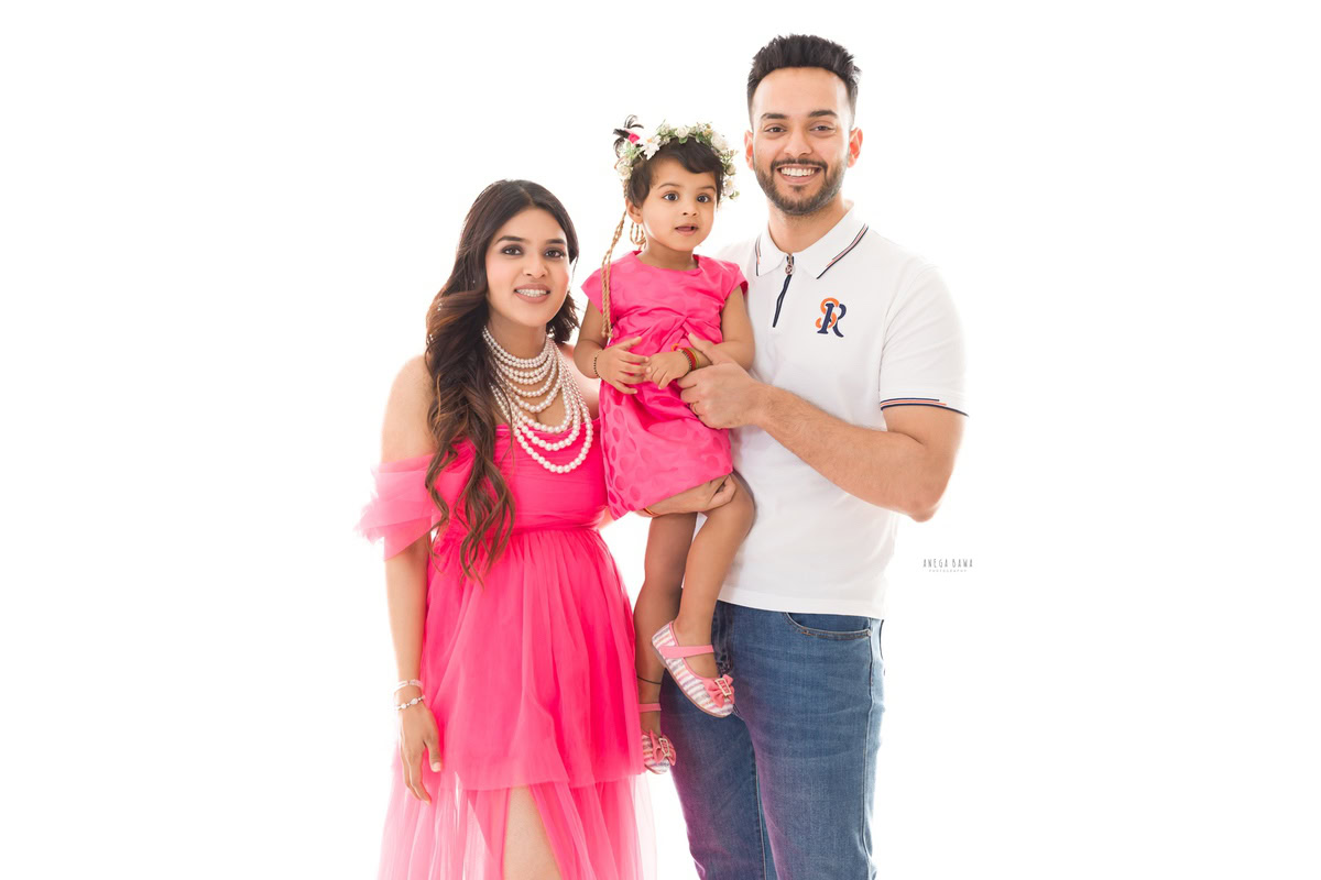 1-year-old girl posing with mom and dad, twinning with mom in a pink dress, against a white backdrop, captured by Anega Bawa Family Photographer Gurgaon (Delhi NCR).