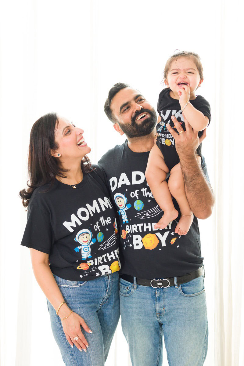 1-year-old girl posing with mom and dad, wearing matching tees against a crisp white backdrop.