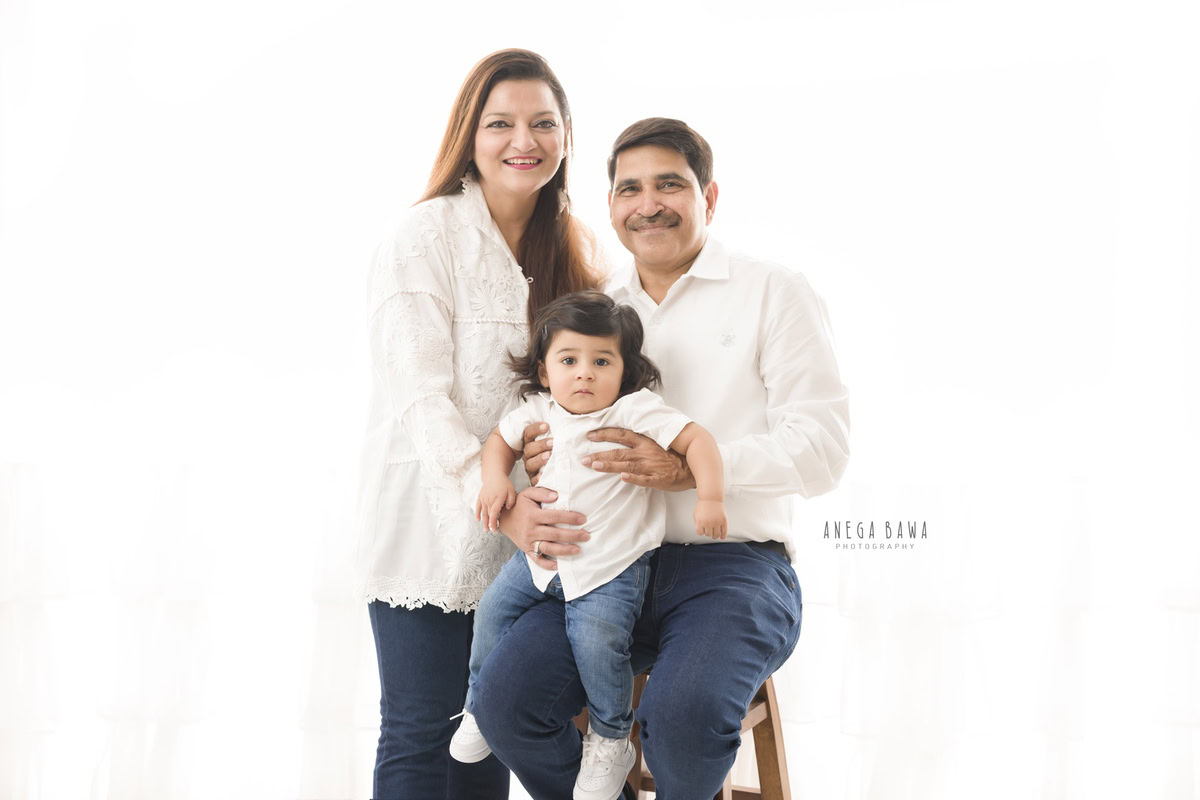 1-year-old girl posing with mom and dad, both wearing stylish white and blue denim outfits, against a clean white backdrop. Captured by Anega Bawa Photography for a family photoshoot in Gurgaon (Delhi NCR).