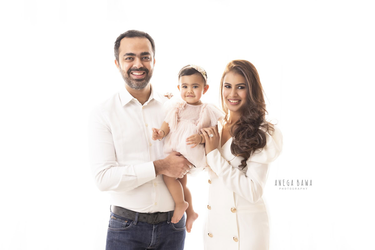 1-year-old girl posing with mom and dad against a white backdrop, captured beautifully by Anega Bawa Photography for a family photoshoot in Gurgaon (Delhi NCR).