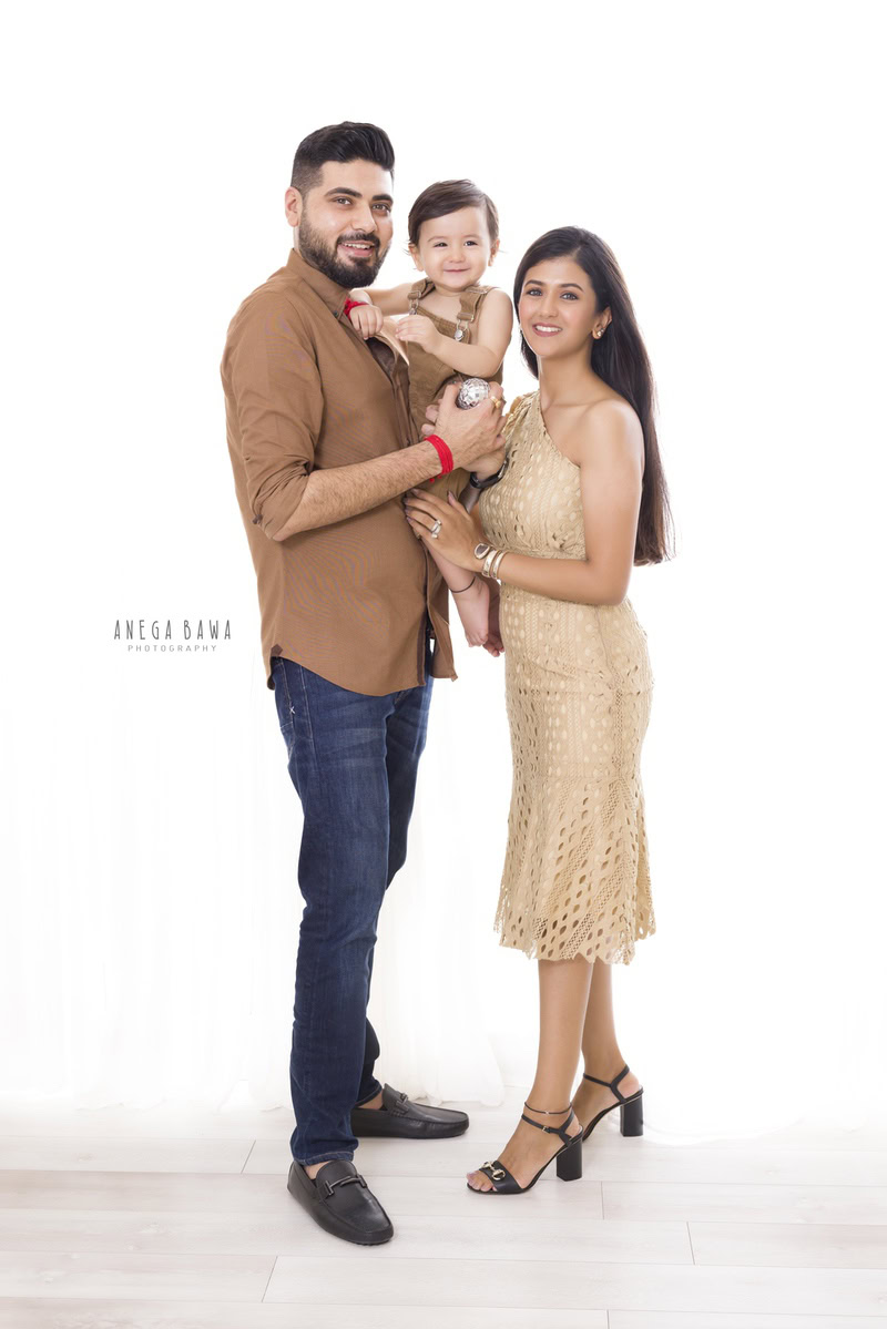 1-year-old girl posing with mom and dad against a white backdrop, captured by Anega Bawa Family Photographer Gurgaon (Delhi NCR).