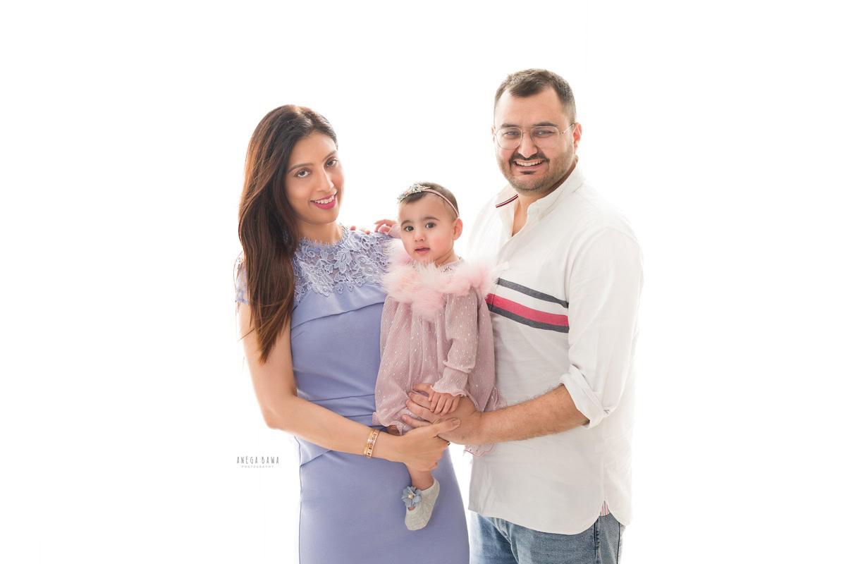 1-year-old girl posing with mom and dad against a serene white backdrop, captured by Anega Bawa Family Photography in Gurgaon (Delhi NCR).