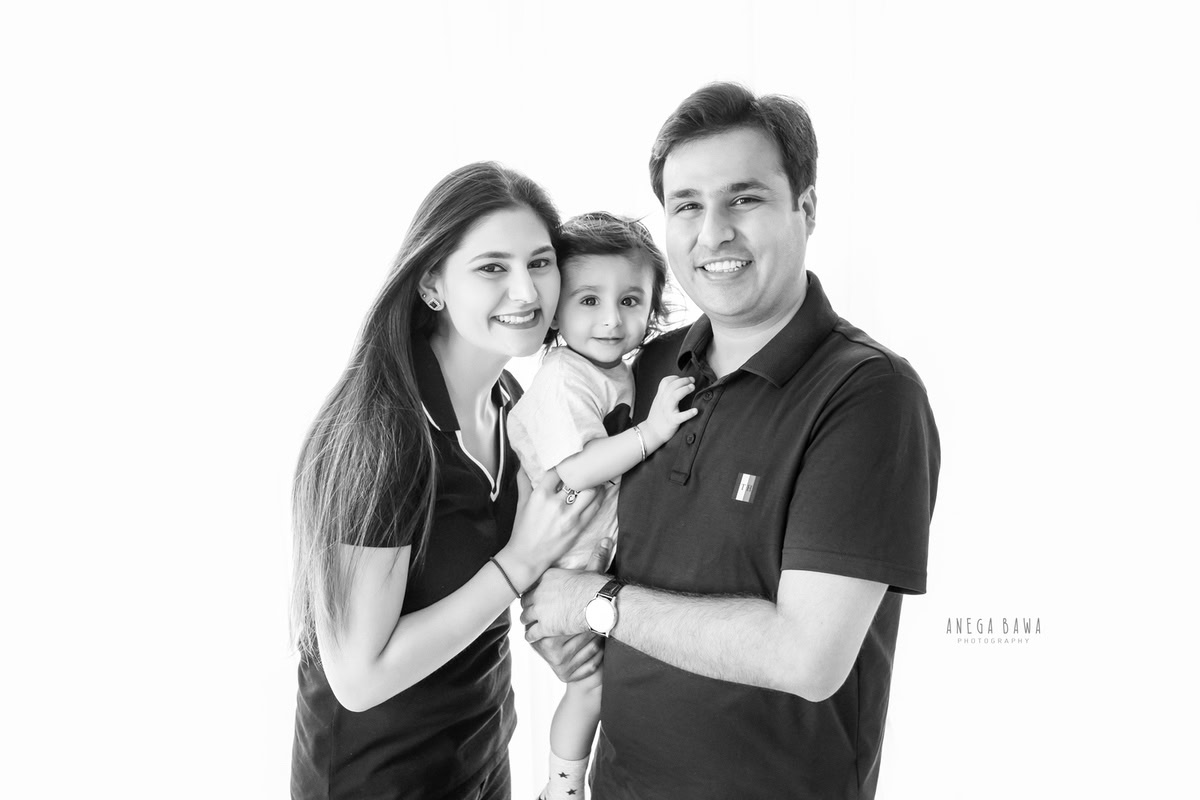 1-year-old girl posing with mom and dad against a white backdrop, captured by Anega Bawa Family Photographer Gurgaon (Delhi NCR).