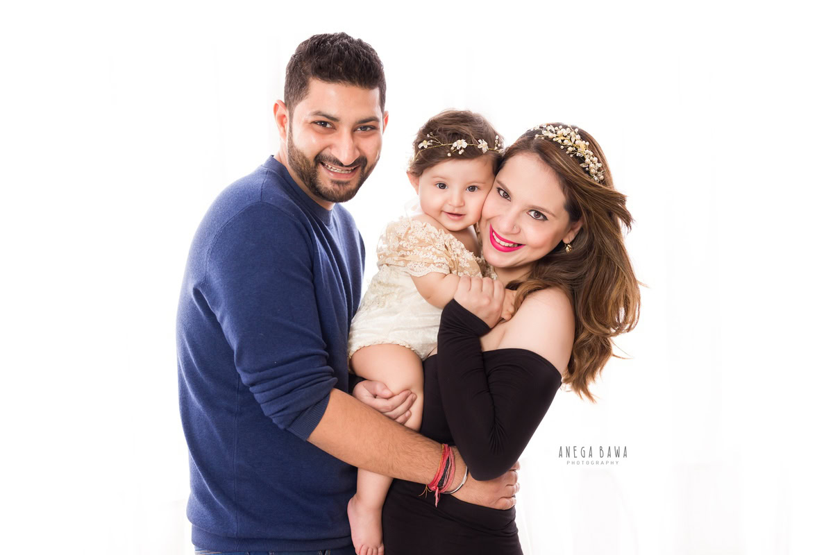 1-year-old girl posing with mom and dad against a white backdrop, captured by Anega Bawa Family Photographer Gurgaon (Delhi NCR).
