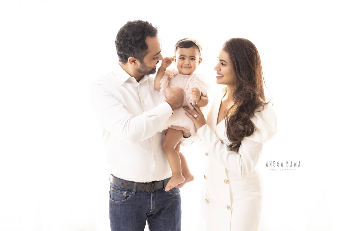 1-year-old girl posing with mom and dad in a smiling pose against a white backdrop, family photoshoot by Anega Bawa, Gurgaon (Delhi, NCR)