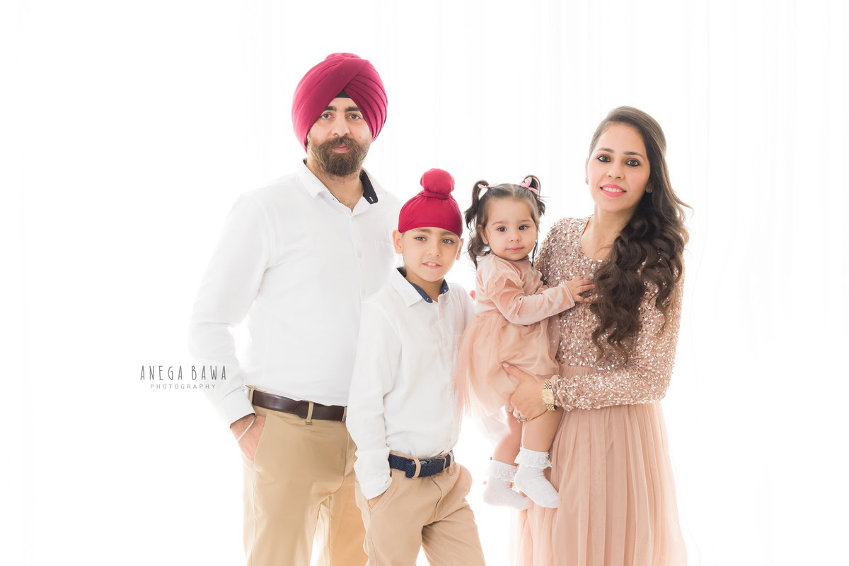 1-year-old girl posing with mom, elder brother, and dad in a family pose against a white backdrop, captured by Anega Bawa, family photographer in Gurgaon (Delhi NCR).