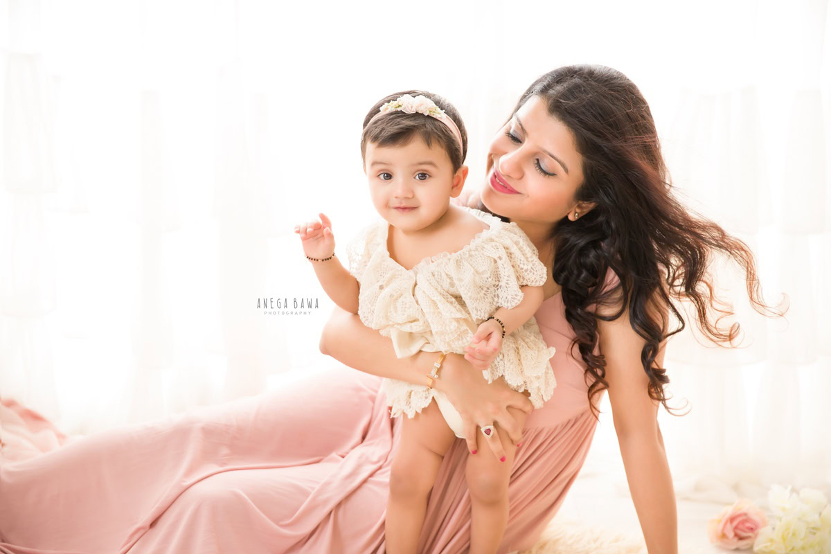 1-year-old girl posing with mom with flowers on the floor against a white backdrop, captured by Anega Bawa Family Photographer Gurgaon (Delhi NCR).