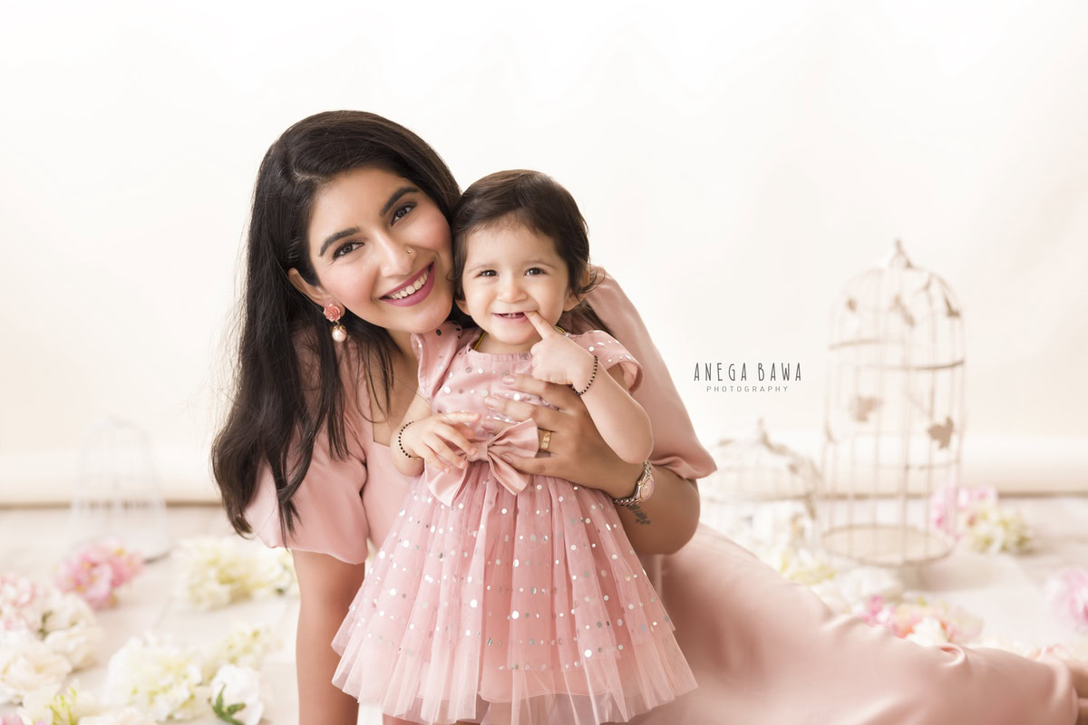 1-year-old girl posing with mom in a peach dress with castles in the background against a white backdrop, captured by Anega Bawa, family photographer in Gurgaon (Delhi NCR).