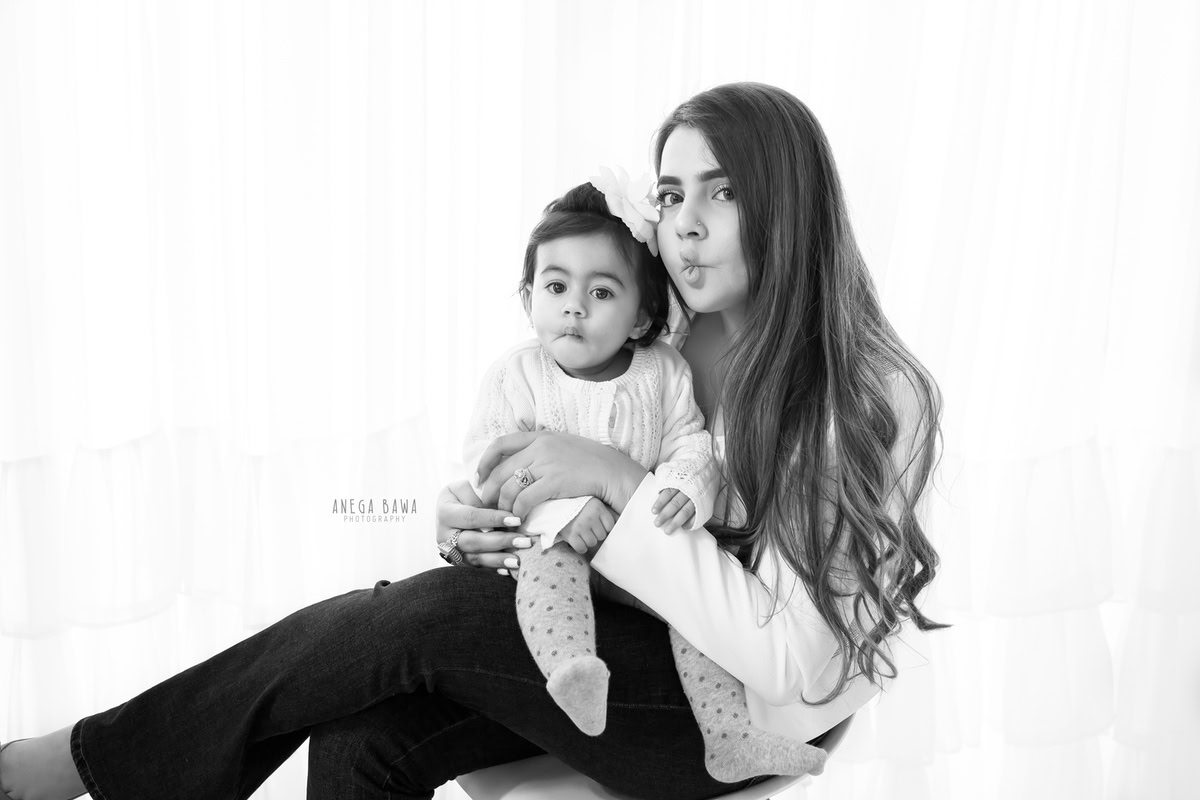 1-year-old girl posing with mom in a pout pose against a white backdrop, captured by Anega Bawa, family photographer in Gurgaon (Delhi NCR).