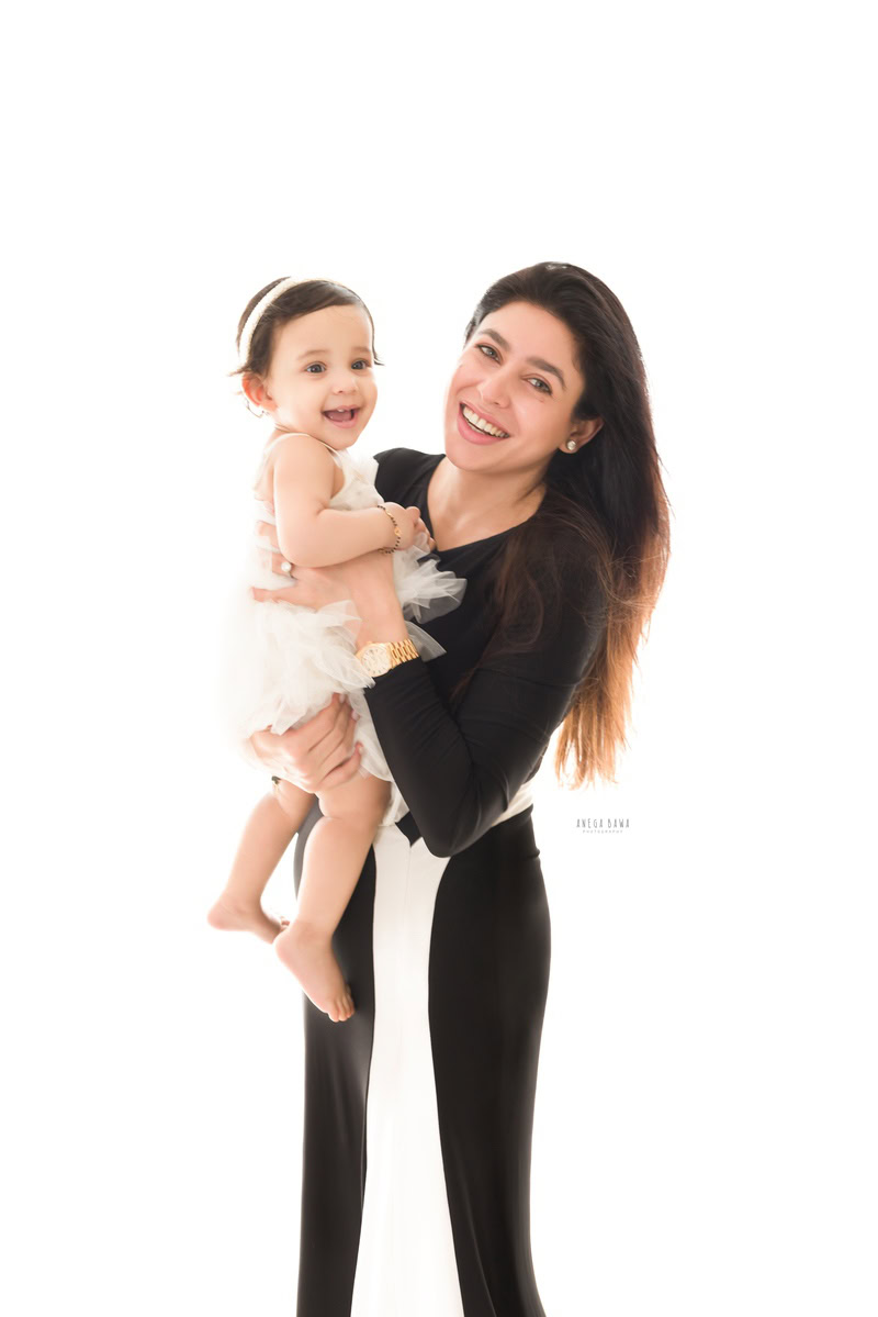 1-year-old girl posing with mom in a smiling pose against a white backdrop, captured by Anega Bawa, family photographer in Gurgaon (Delhi NCR).