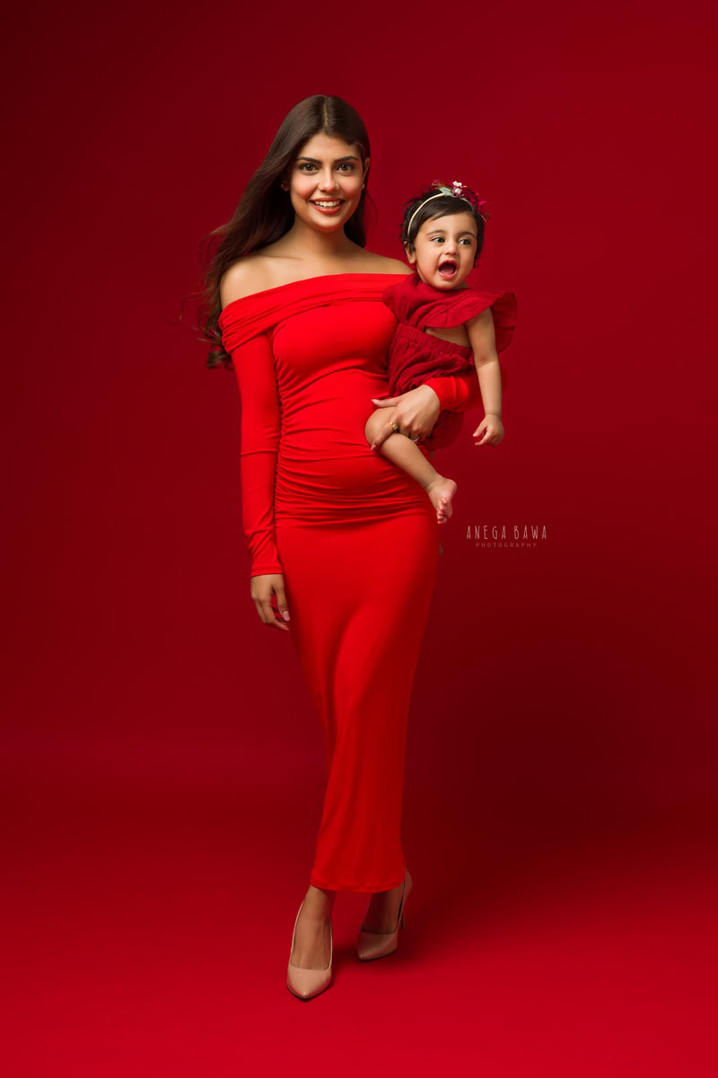 1-year-old girl posing with mom, both twinning in red dresses against a red backdrop, captured by Anega Bawa Family Photographer Gurgaon (Delhi NCR).