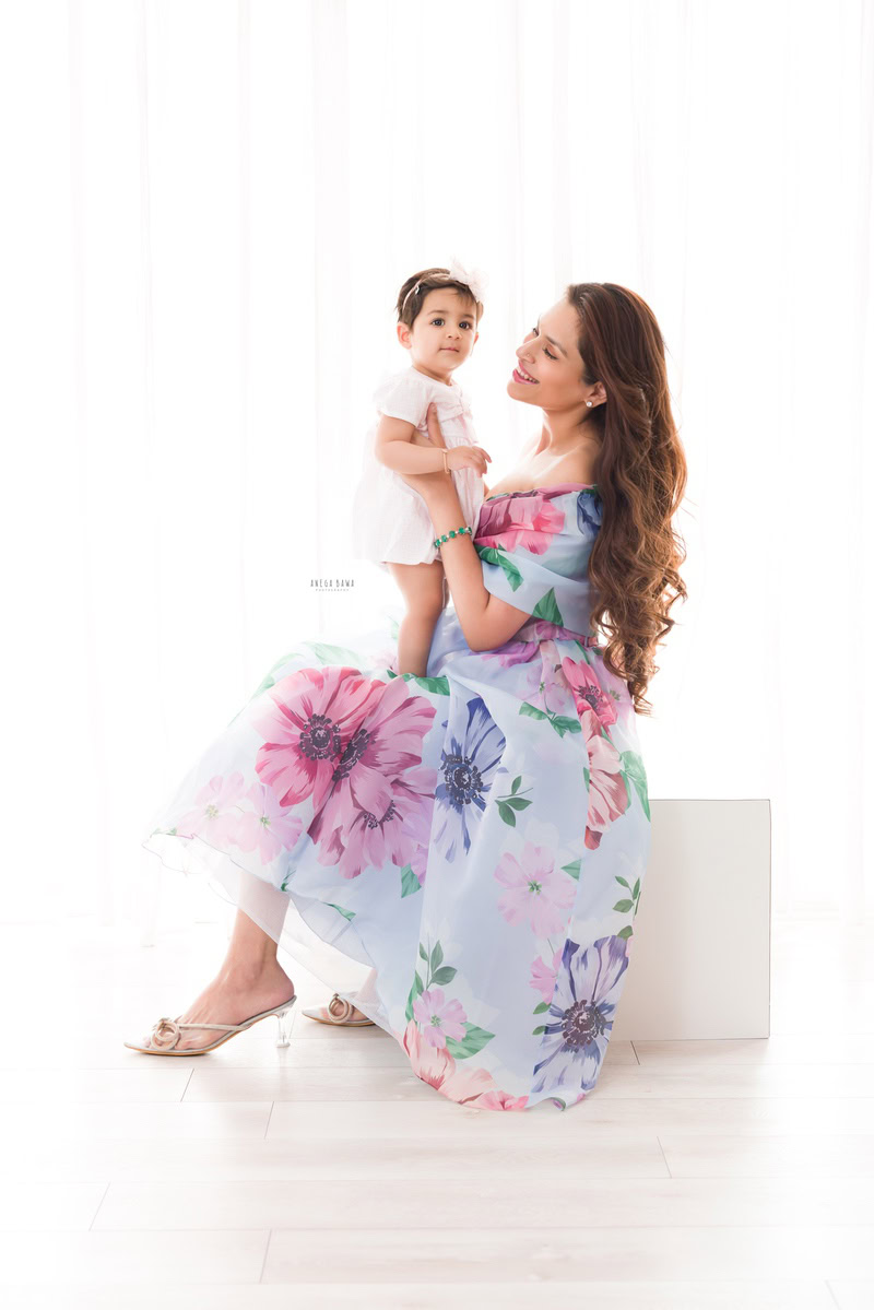 1-year-girl in a floral dress posing with mom against a serene white backdrop, captured by Anega Bawa Photography in Gurgaon (Delhi NCR).