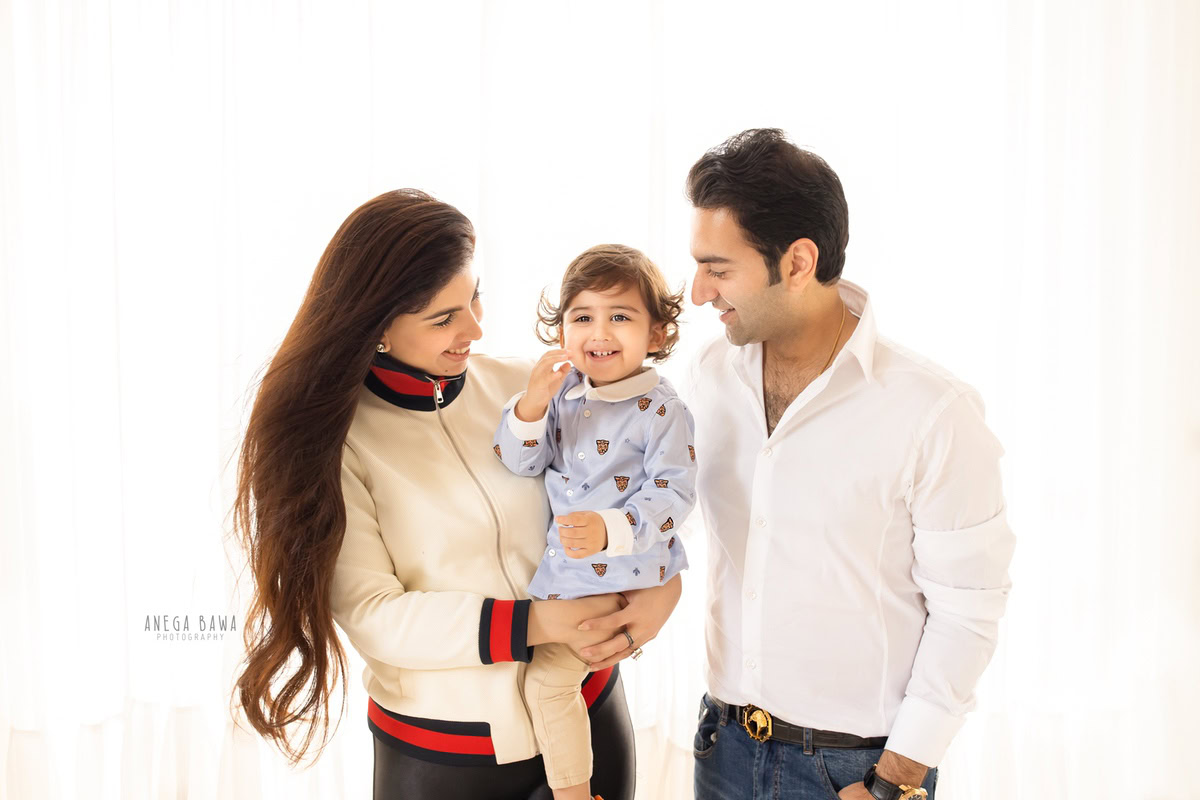 1-year girl smiling cutely with mom and dad against a clean white backdrop, captured by Anega Bawa Photography in Gurgaon (Delhi NCR).