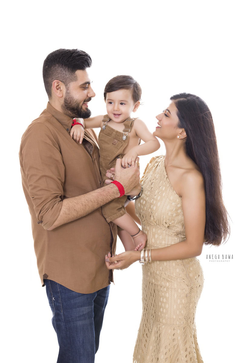 1-year-old girl in a smiling pose with mom and dad against a white backdrop, captured by Anega Bawa, family photographer in Gurgaon (Delhi NCR).