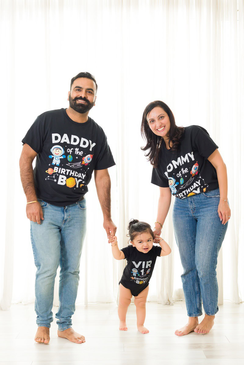 1-year girl standing on the floor with mom and dad against a white backdrop, beautifully captured by Anega Bawa Photography for a photoshoot in Gurgaon (Delhi NCR).