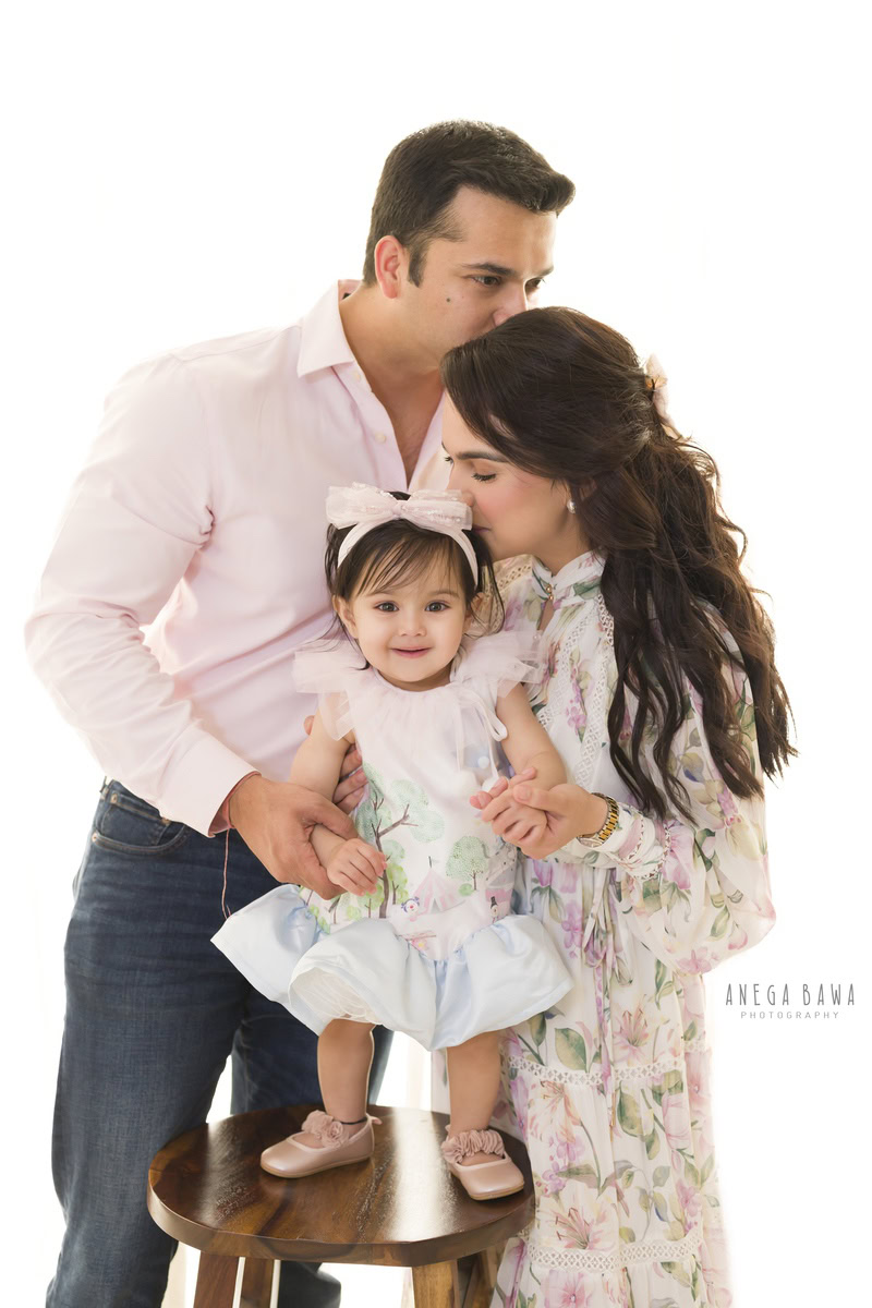 1-year-old girl standing on a wooden stool, striking an adoring pose against a serene white backdrop, captured beautifully by Anega Bawa Photography in Gurgaon (Delhi NCR).