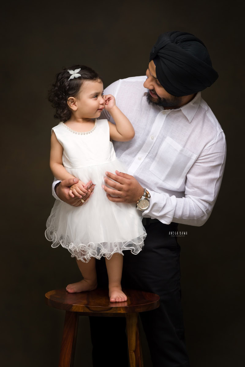 1-year-old girl standing on a wooden stool, posing with dad against a black backdrop, family photoshoot by Anega Bawa, Gurgaon (Delhi, NCR)