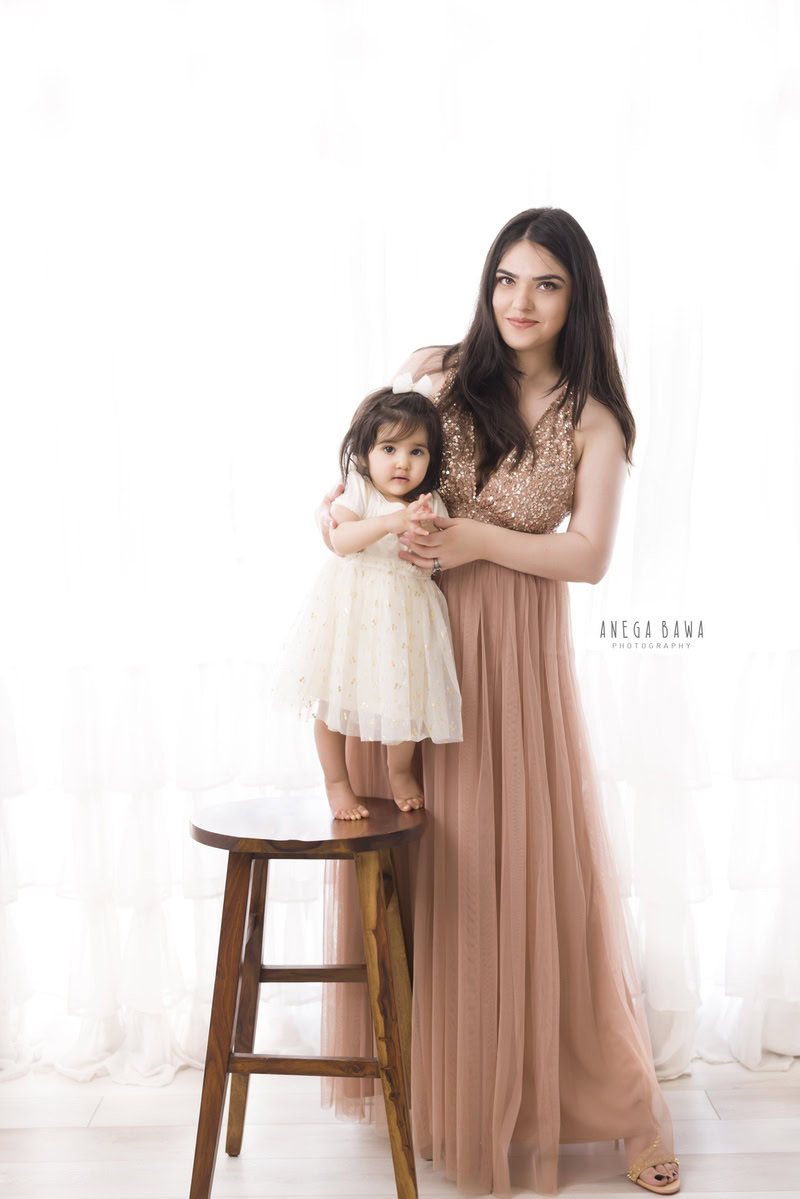 1-year-girl standing on a wooden stool, posing with her mom against a white backdrop, captured beautifully by Anega Bawa Photography in Gurgaon (Delhi NCR).