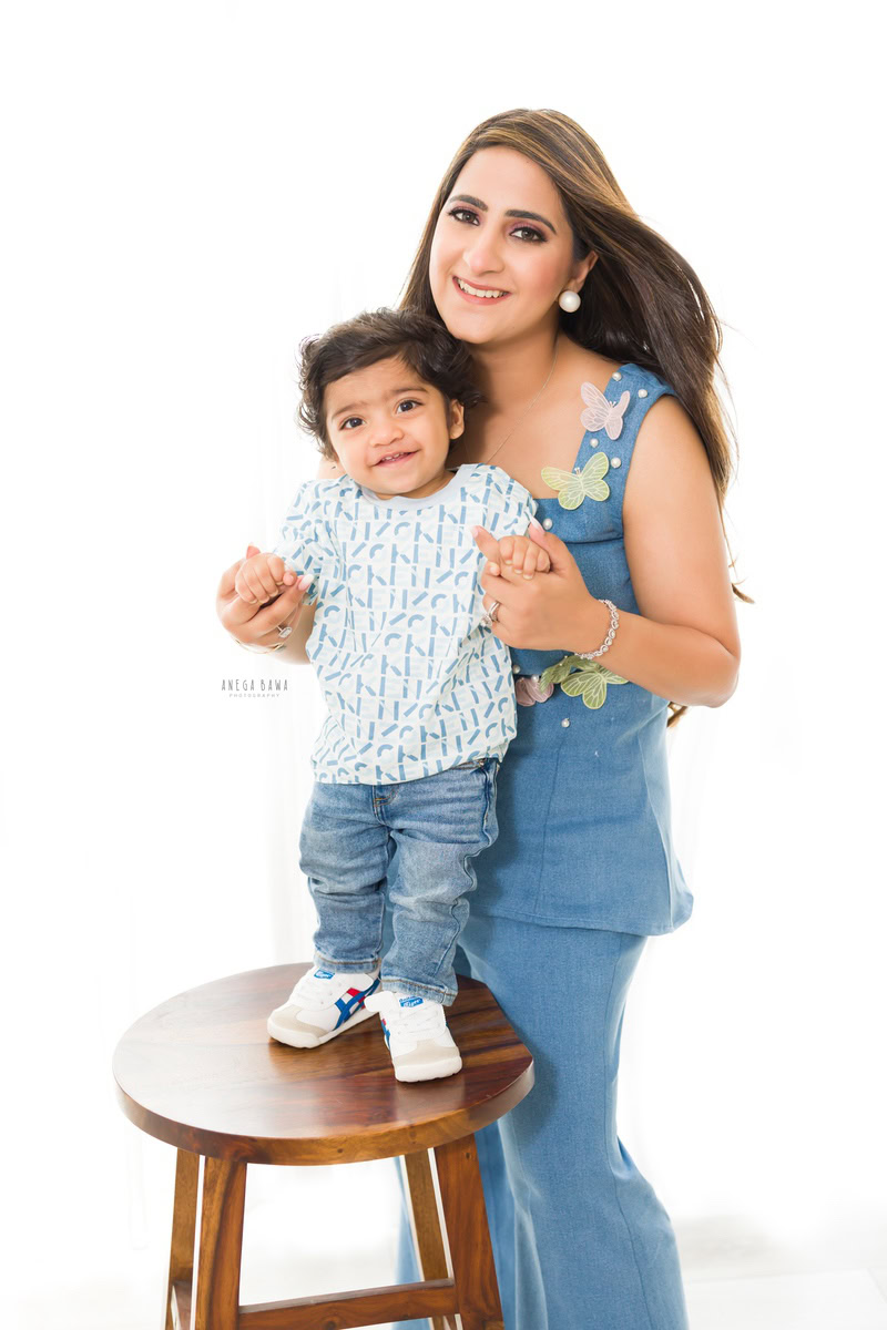 1-year-old girl standing on a wooden stool, posing with mom against a white backdrop, captured by Anega Bawa, family photographer in Gurgaon (Delhi NCR).