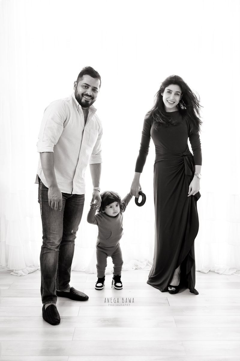 1-year-old son delicately holding mom and dad's hands, striking a pose against a pristine white backdrop. Expertly captured by Anega Bawa Photography, Gurgaon (Delhi, NCR).