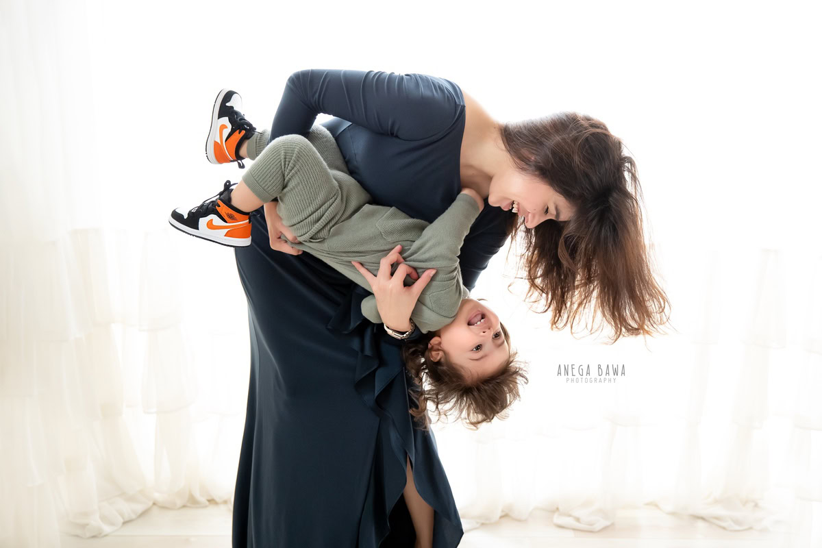 1-year-old son playfully interacting with mom against a serene white backdrop. Professionally captured by Anega Bawa Photography, Gurgaon (Delhi, NCR).