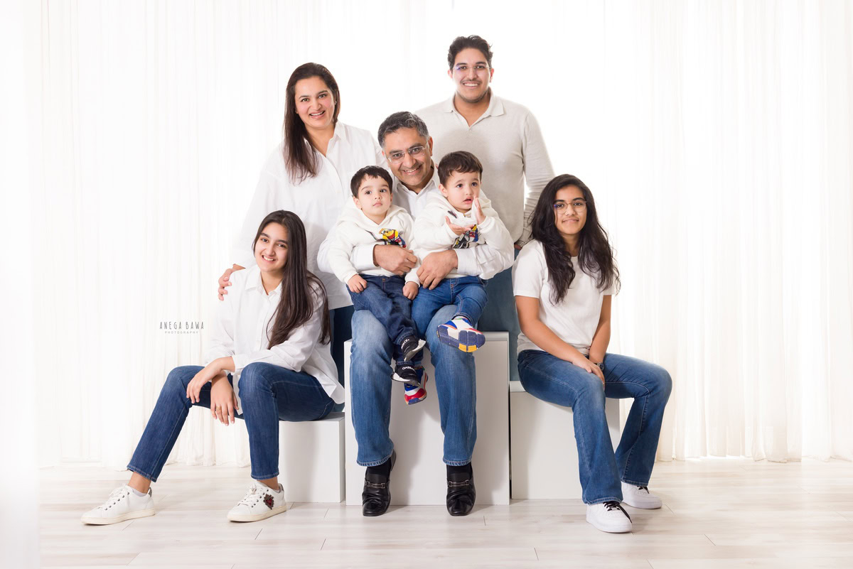 1-year-old twin boys seated on grandfather's lap, with mom, dad, elder sister, and granny in a family pose, all wearing white against a white backdrop, family photoshoot by Anega Bawa, Gurgaon (Delhi, NCR)