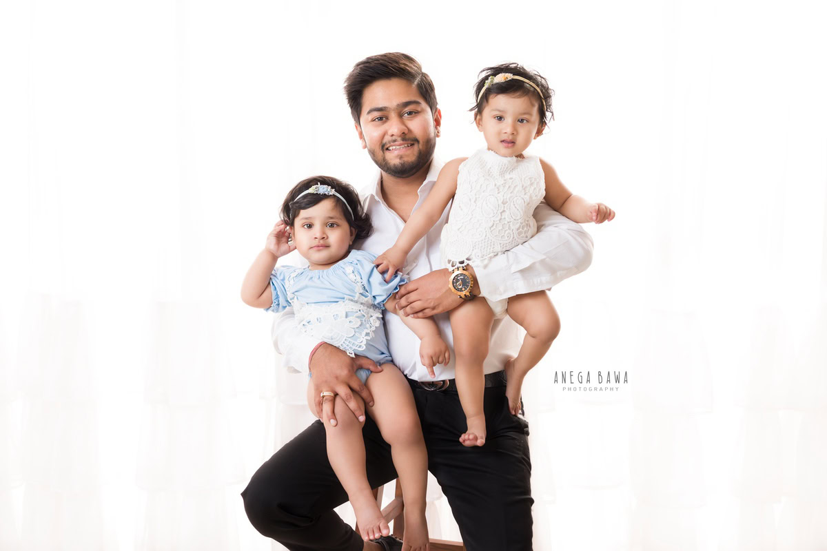 Twin 1-year-old girls posing with dad against a crisp white backdrop, captured beautifully by Anega Bawa Photography for a family photoshoot in Gurgaon, Delhi NCR.