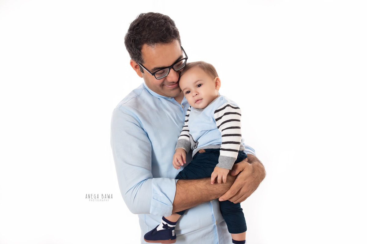10-month-old boy joyfully cradled in dad's arms against a pristine white backdrop, captured in a family photoshoot by Anega Bawa, Gurgaon (Delhi, NCR)