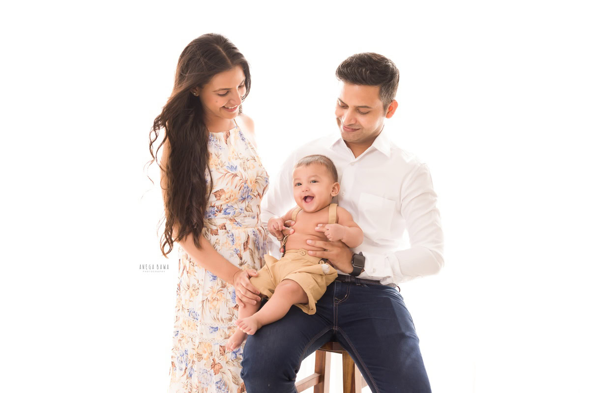 10-month-old boy laughing with mom and dad in a pose against a white backdrop, captured by Anega Bawa family photographer Gurgaon (Delhi NCR).