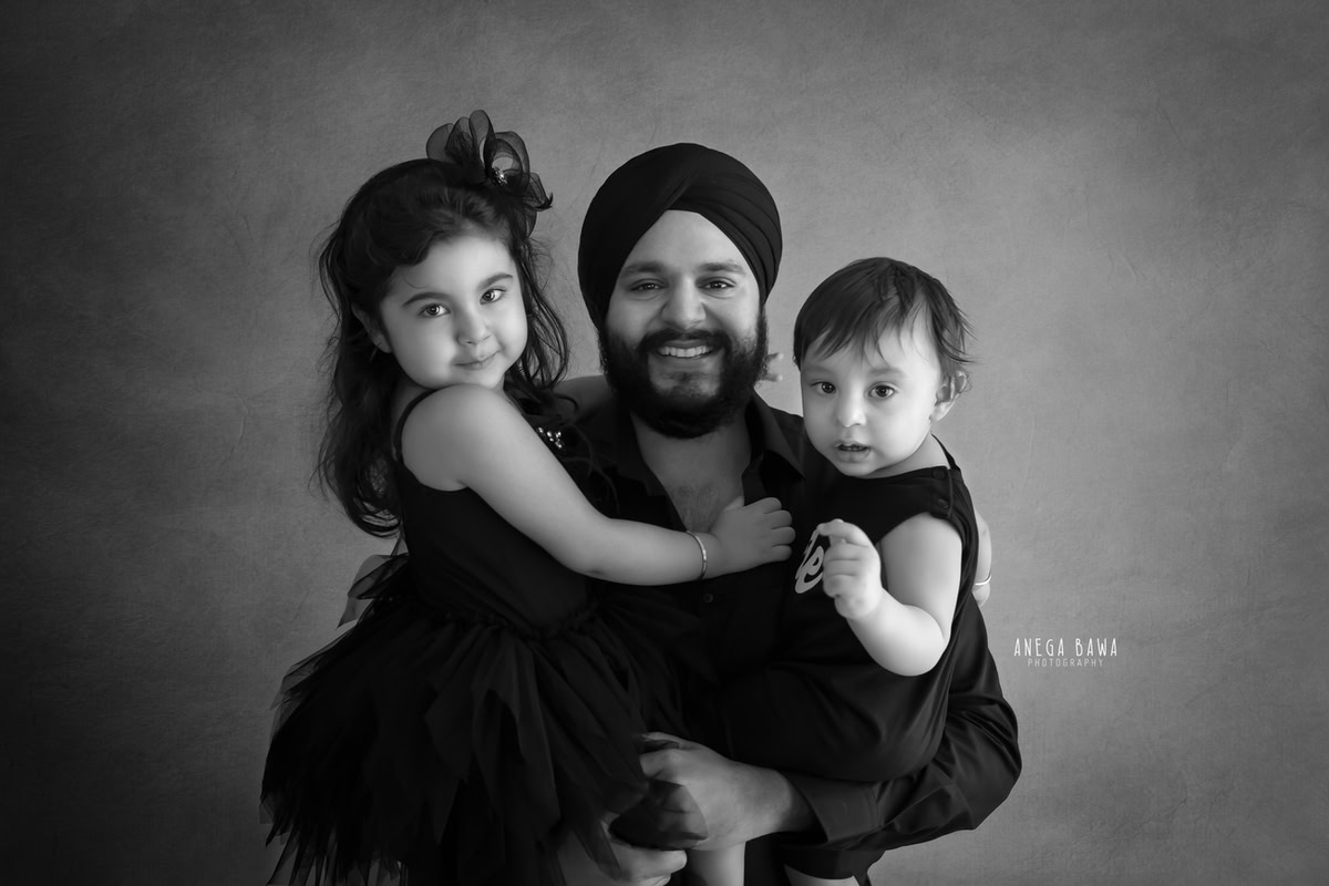 10-months-boy posing cute with elder sister against a serene white backdrop, captured during a family photoshoot by Anega Bawa in Gurgaon (Delhi NCR).
