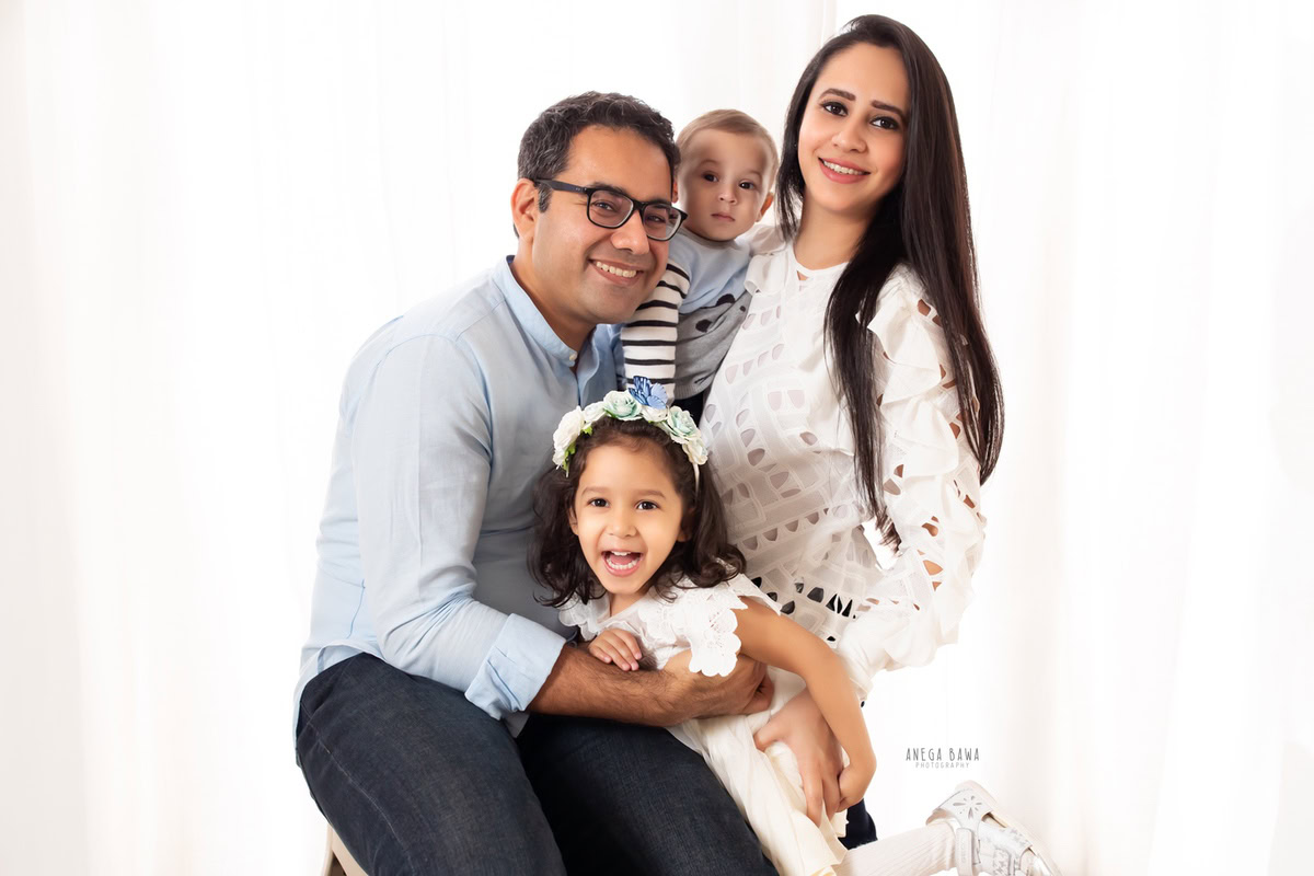 10-month-old boy posing with elder sister, mom, and dad against a clean white backdrop, in a heartwarming family portrait by Anega Bawa, Gurgaon (Delhi, NCR)