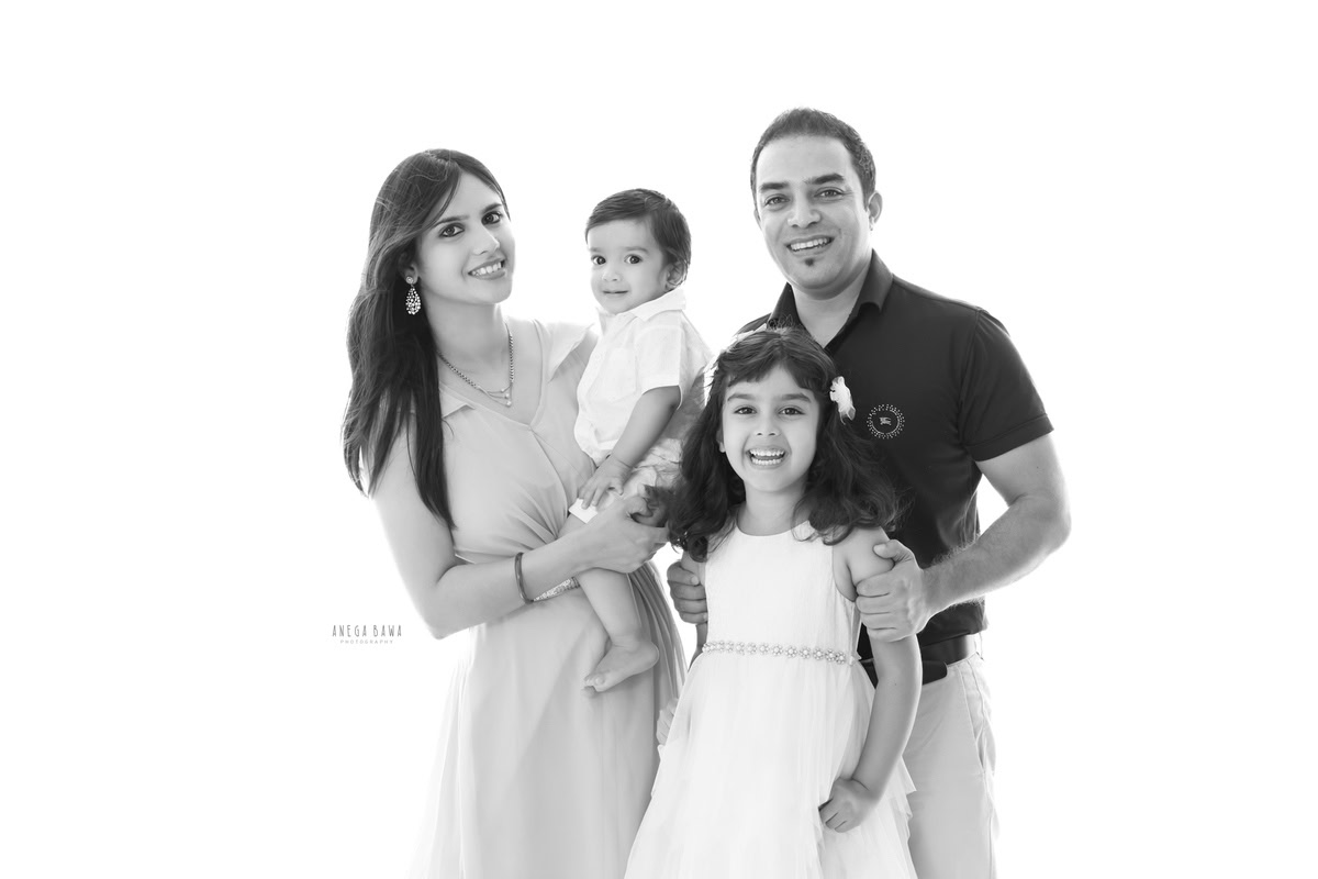 10-month-old boy posing with mom, elder sister, and dad in a family portrait against a clean white backdrop, captured by Anega Bawa in Gurgaon (Delhi, NCR)