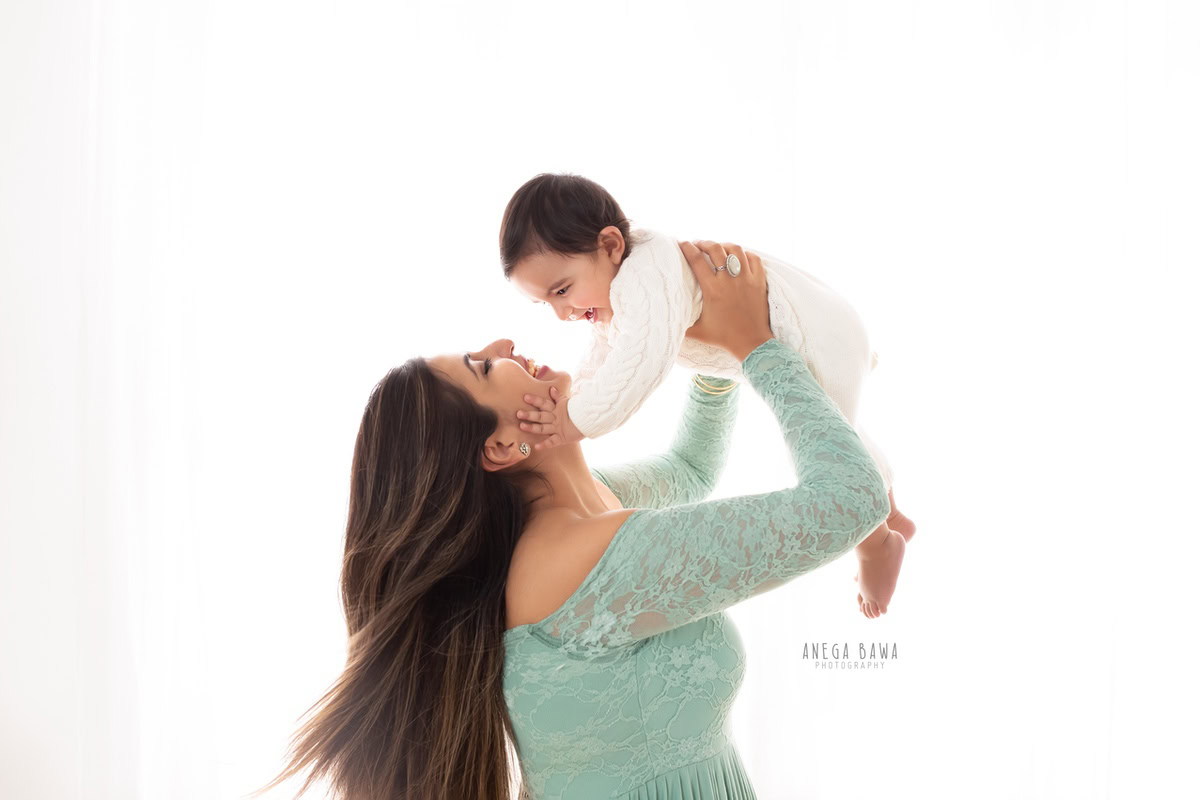 10-months boy playing with mom in a posed moment against a white backdrop, captured by Anega Bawa Family Photographer in Gurgaon (Delhi NCR).