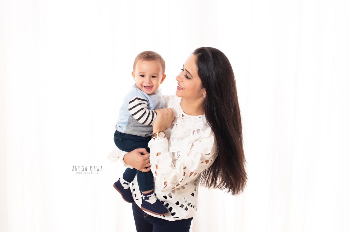 10-months-boy posing with mom in a smiling pose against a white backdrop, captured by Anega Bawa Photography for a family photoshoot in Gurgaon (Delhi NCR).
