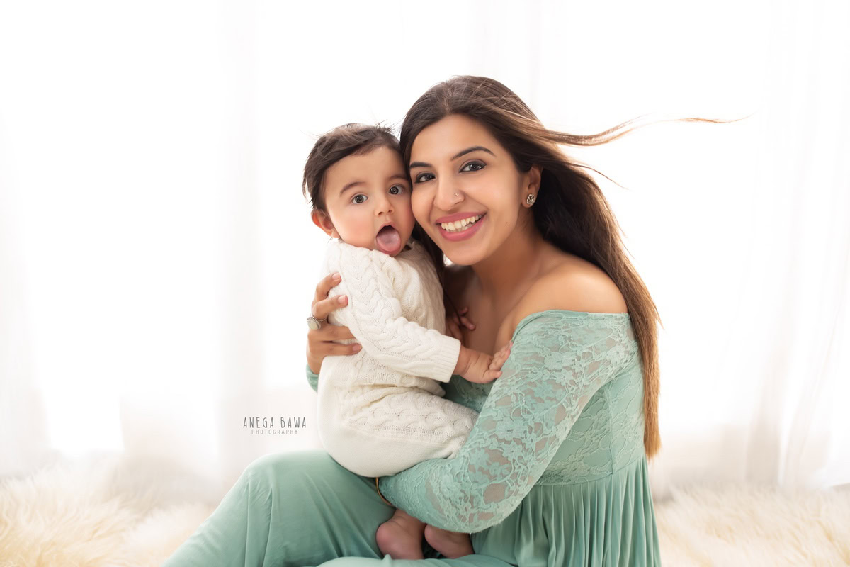10-months-boy posing with mom against a serene white backdrop, beautifully captured by Anega Bawa Photography for a family photoshoot in Gurgaon (Delhi NCR).