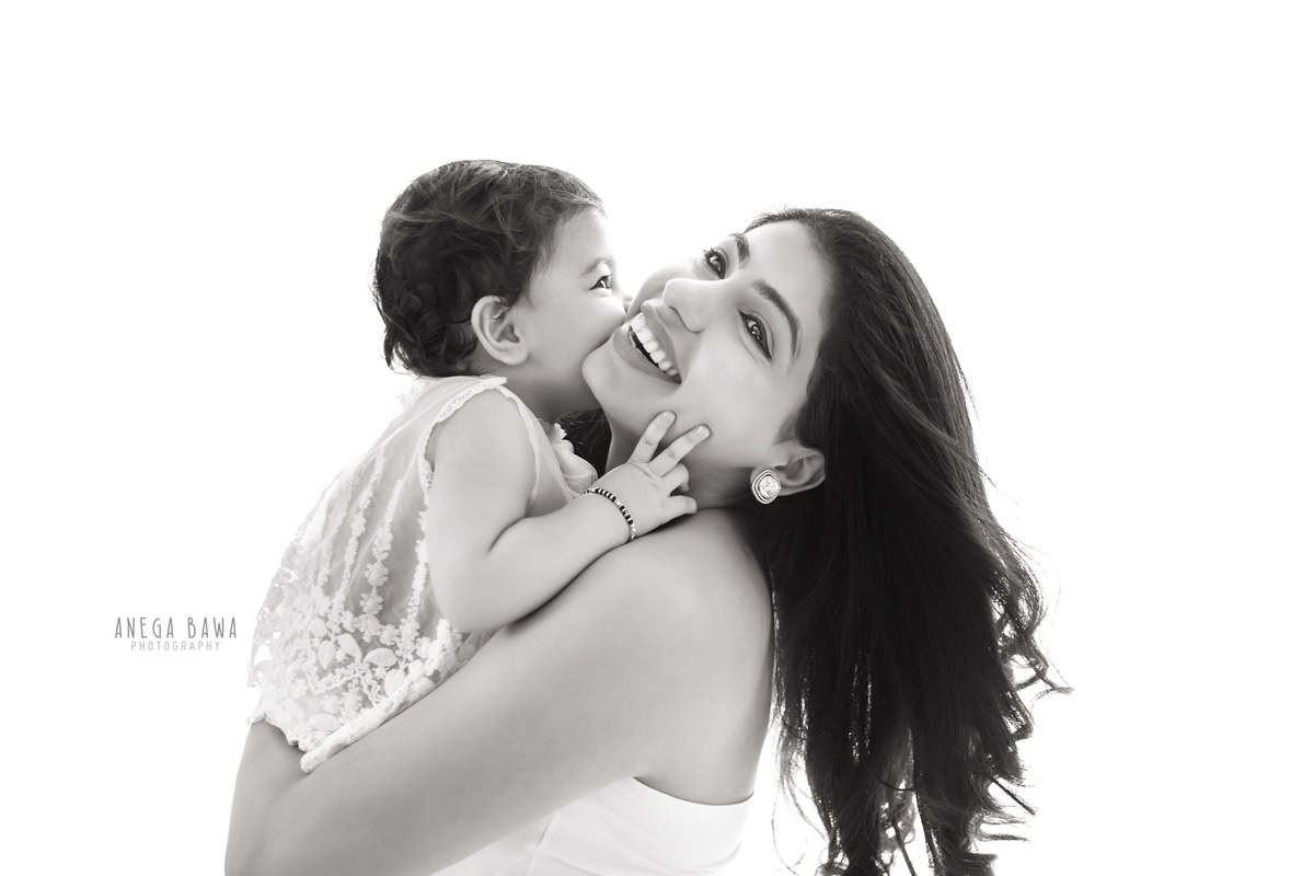 10-months-girl lovingly poses with mom in a cute pose against a serene white backdrop, captured by Anega Bawa Photography for a family photoshoot in Gurgaon (Delhi NCR)