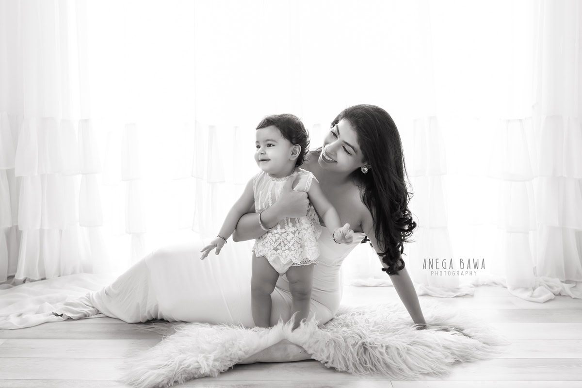 10-month-old girl posing cutely with mom on a white backdrop and beige rug, captured by Anega Bawa family photographer Gurgaon (Delhi NCR).